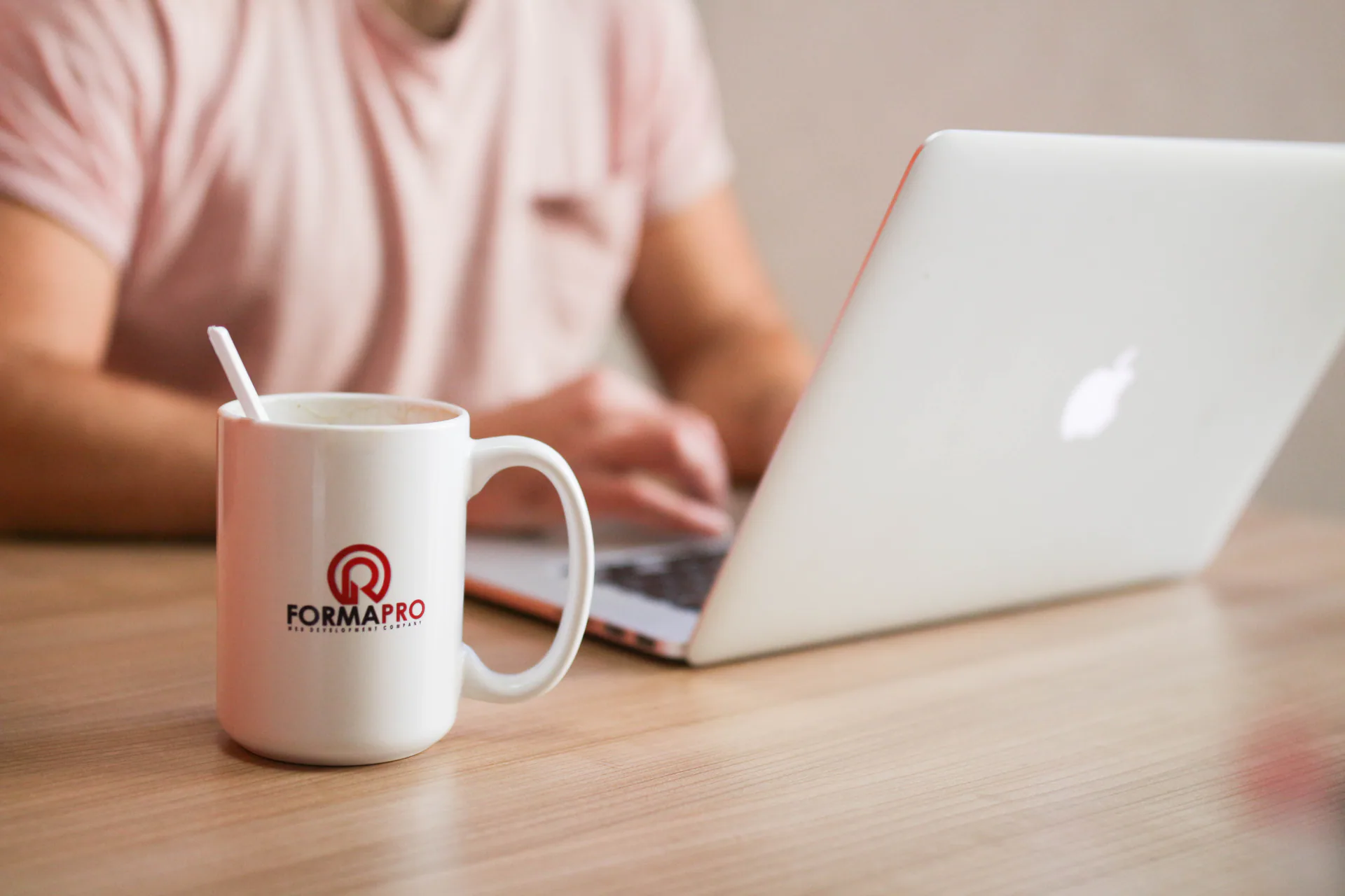 A person working at a laptop beside a Forma Pro mug.