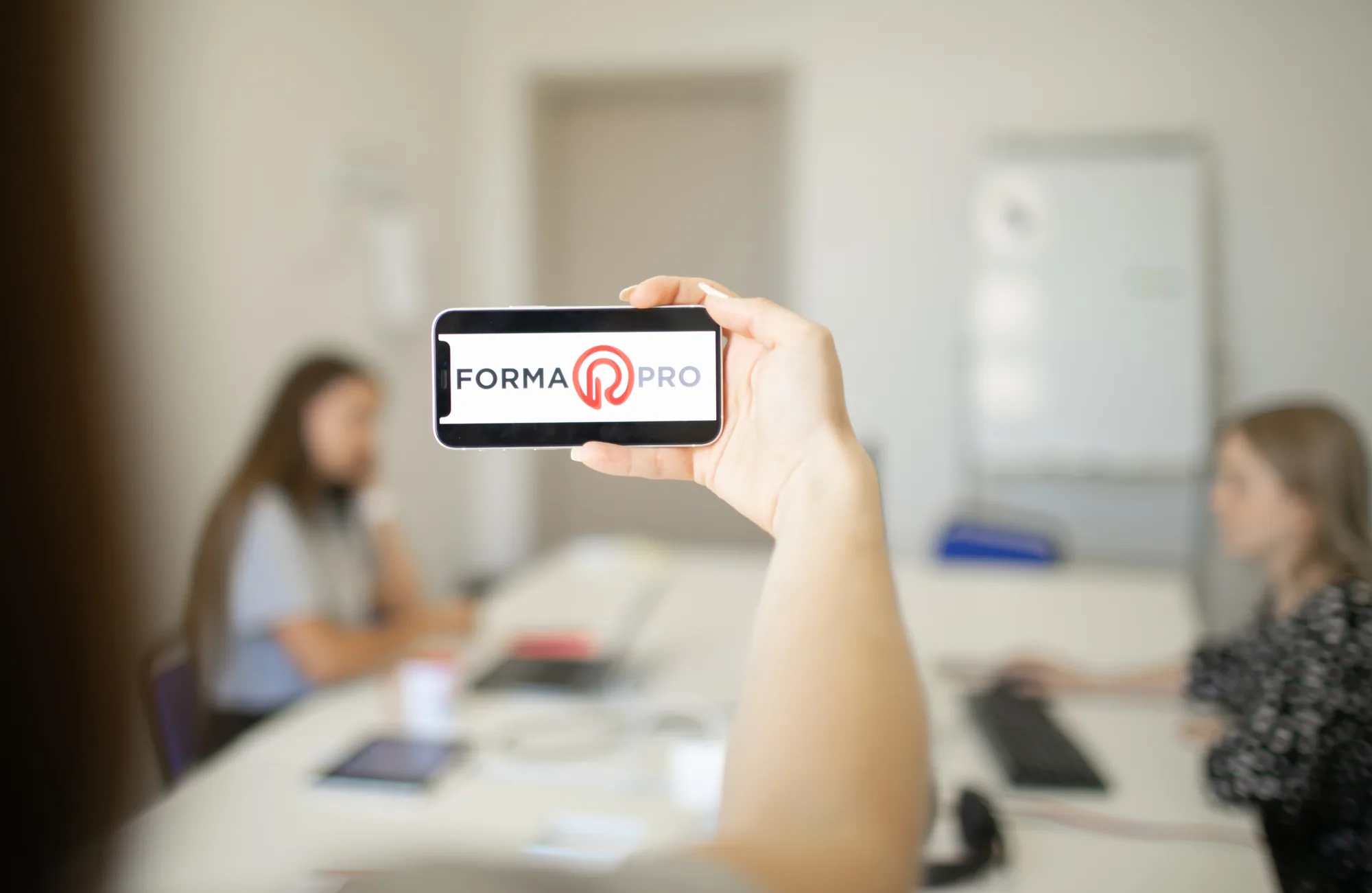Smartphone displaying the Forma Pro logo in a softly blurred office